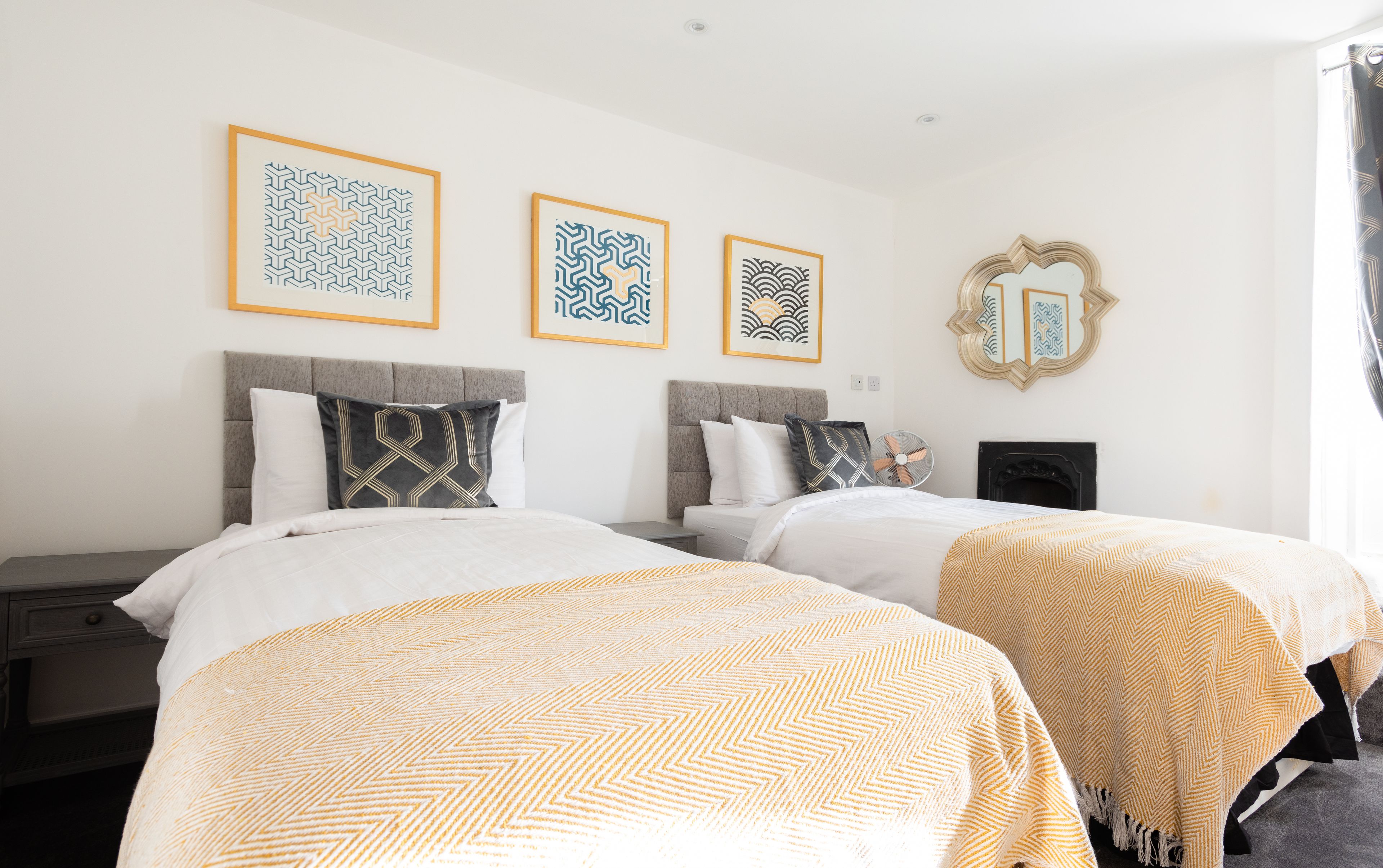 A hotel room with two beds, a fireplace, and three framed artworks on the wall.