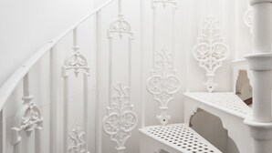 A white staircase with ornate metal railings and a white bench at the bottom. - The Marylebone Residence (London)
