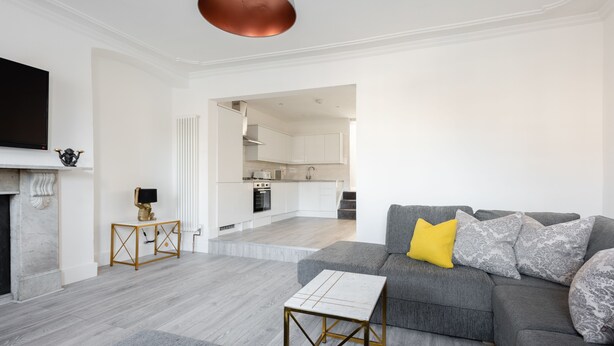 A modern living room with a grey sofa, a coffee table, and a TV mounted on the wall. - The Marylebone Residence (London)