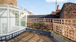 A conservatory with a wooden deck, a brick wall, and a metal fence. - The Marylebone Residence (London)