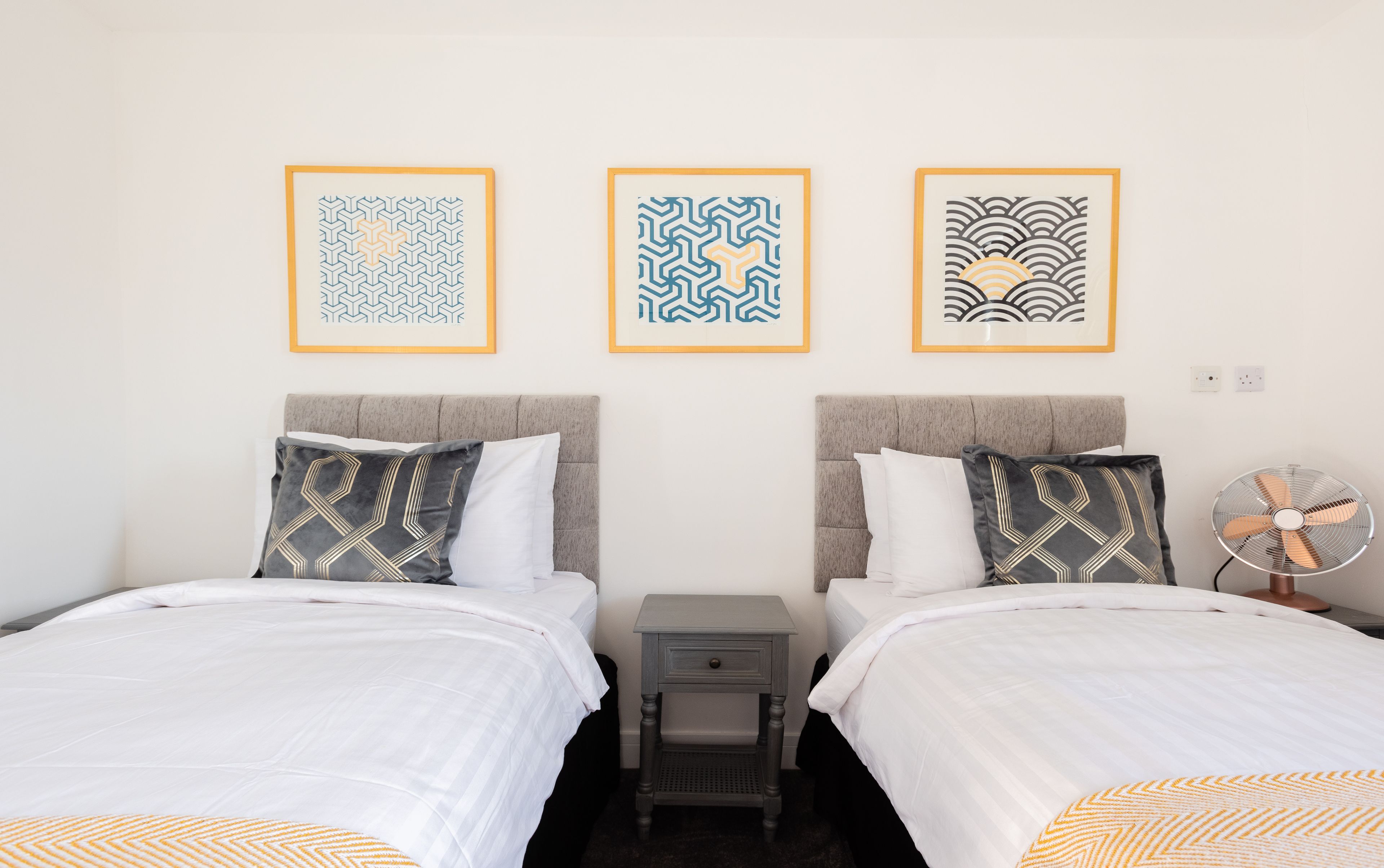 A hotel room with two beds, a nightstand, and a wall-mounted fan.