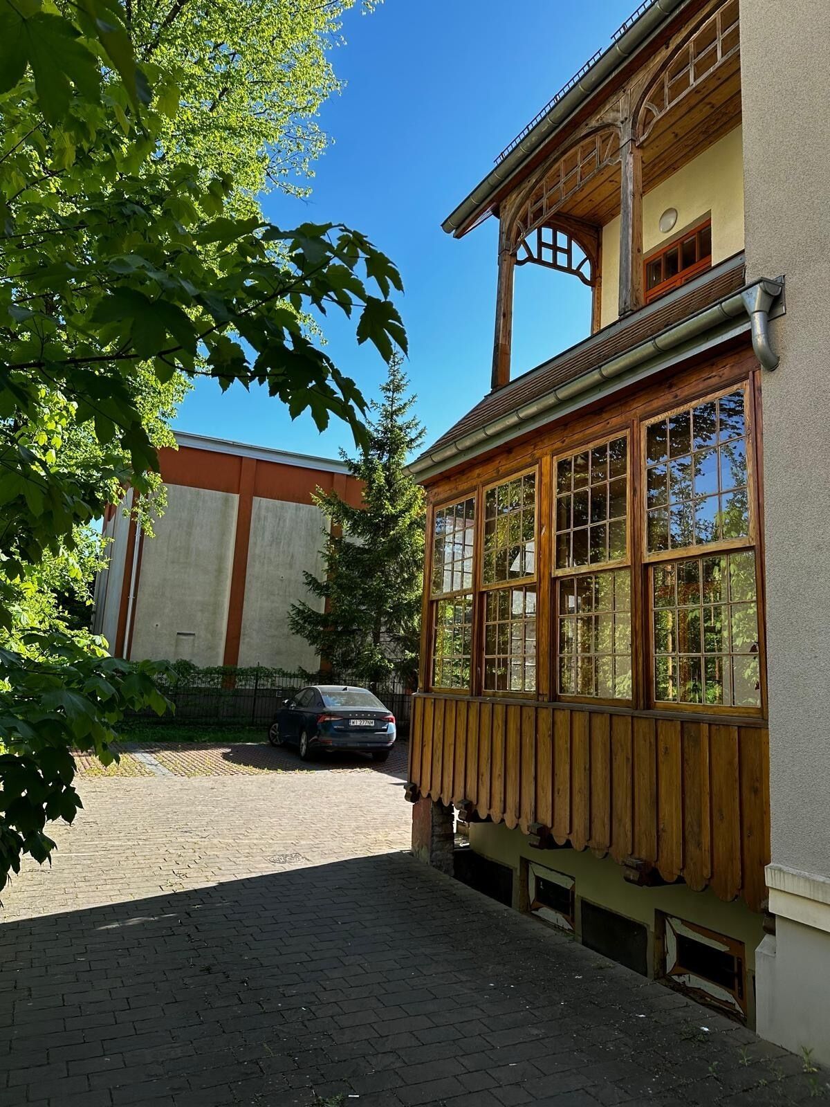Un bâtiment doté d’une façade en bois et de grandes fenêtres, une voiture garée devant, et une allée pavée.