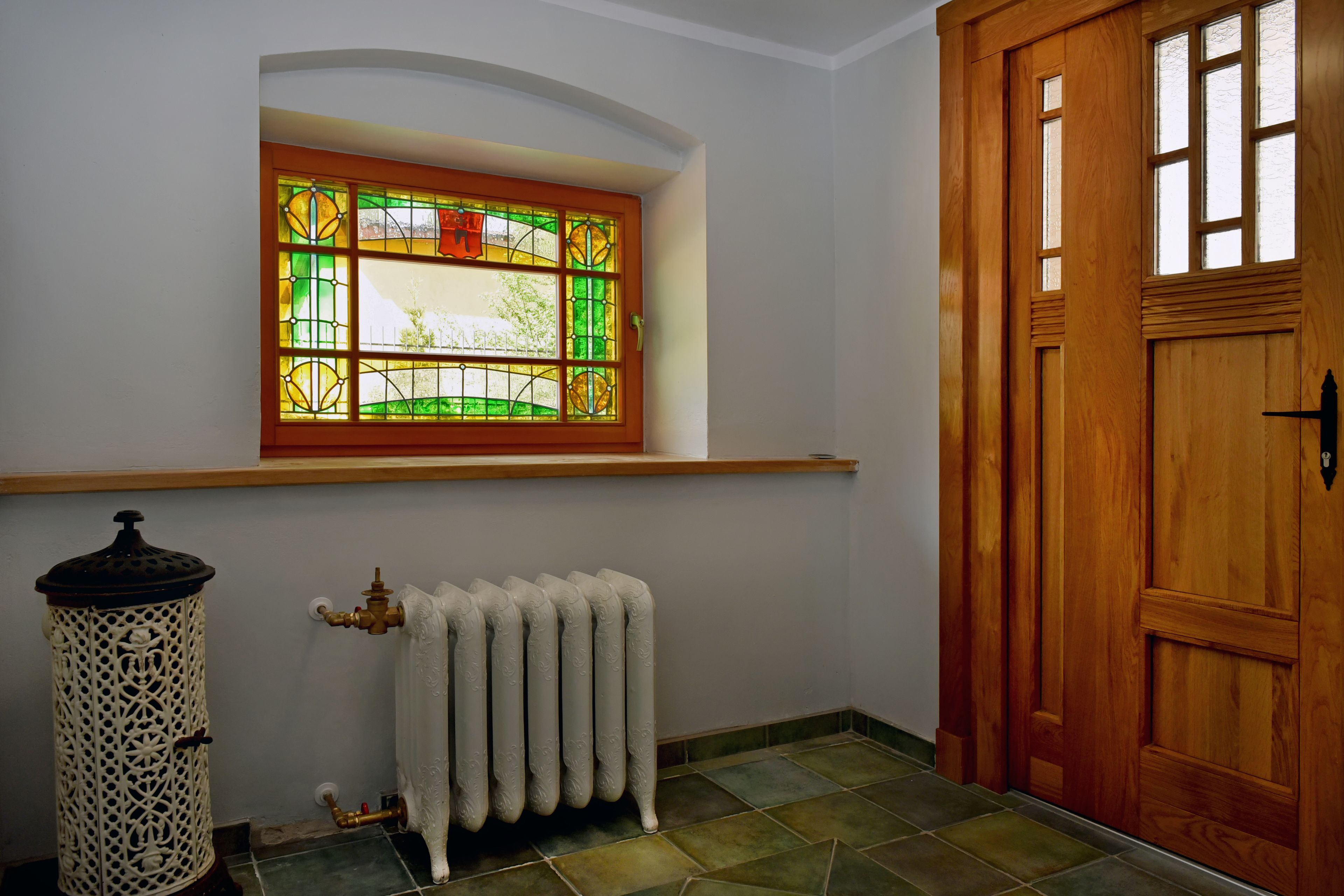 Een kamer met een houten deur, een radiator en een glas-in-loodraam.