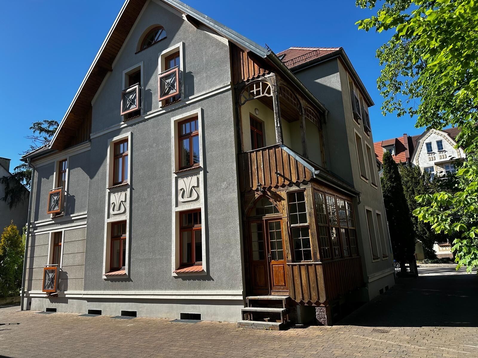 Un edificio de dos pisos con fachada gris, varias ventanas y un balcón de madera.