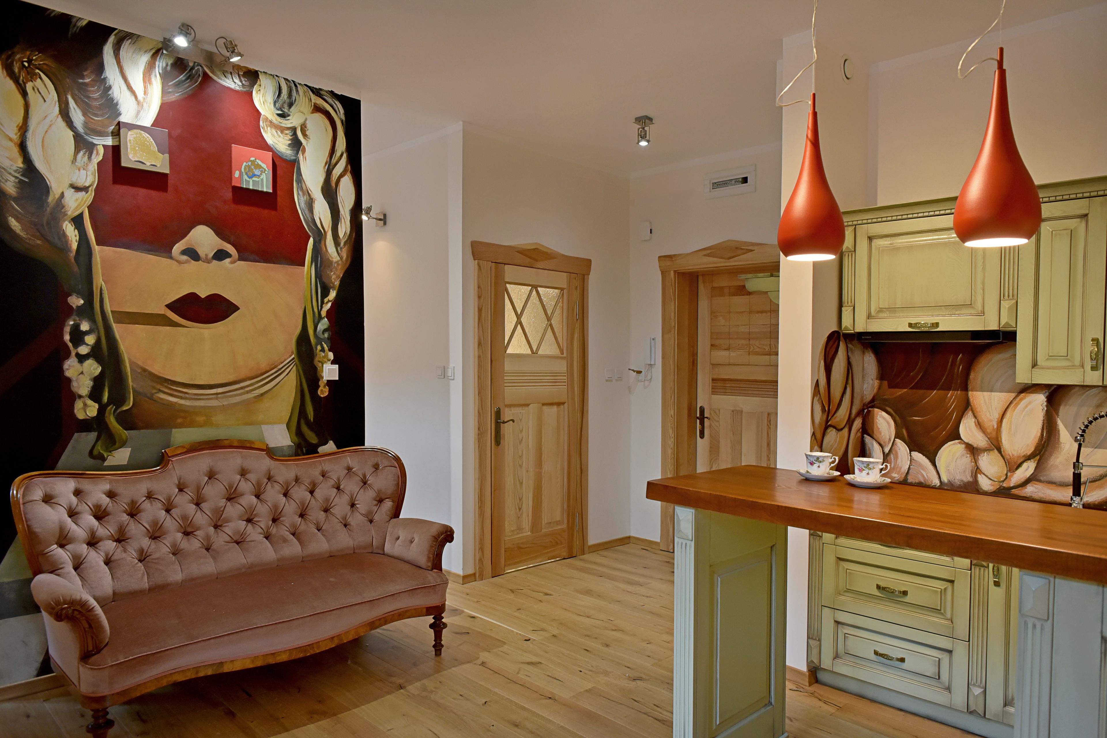 Una habitación con piso de madera, un sofá, una zona de cocina con muebles de madera y una puerta con un diseño geométrico.