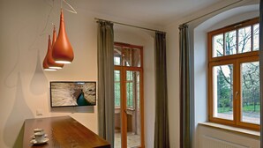Una habitación con una mesa de madera, un televisor montado en la pared, una ventana con cortinas y una puerta que da a un área exterior.