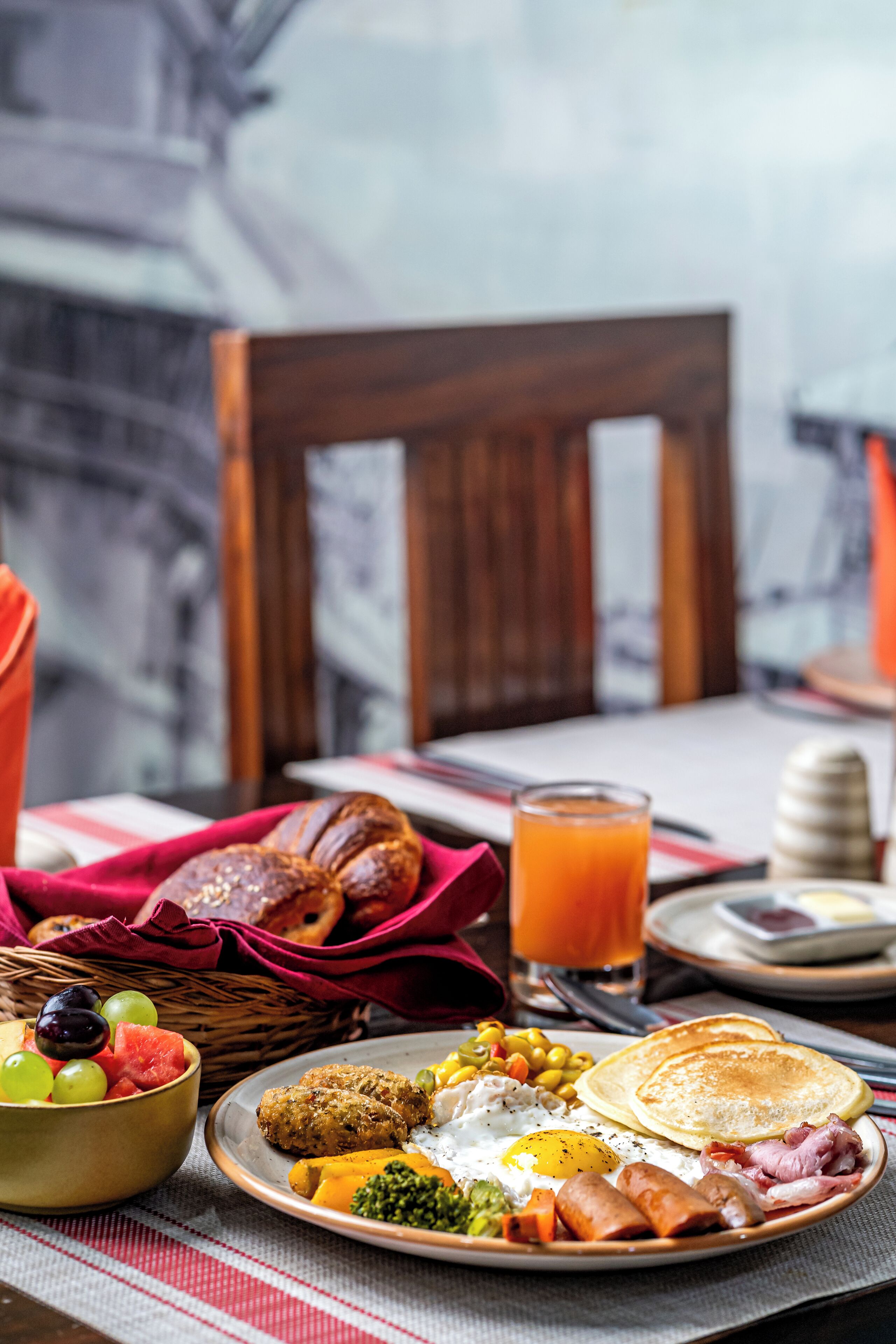A breakfast table with a variety of foods including eggs, sausages, toast, and a glass of orange juice.