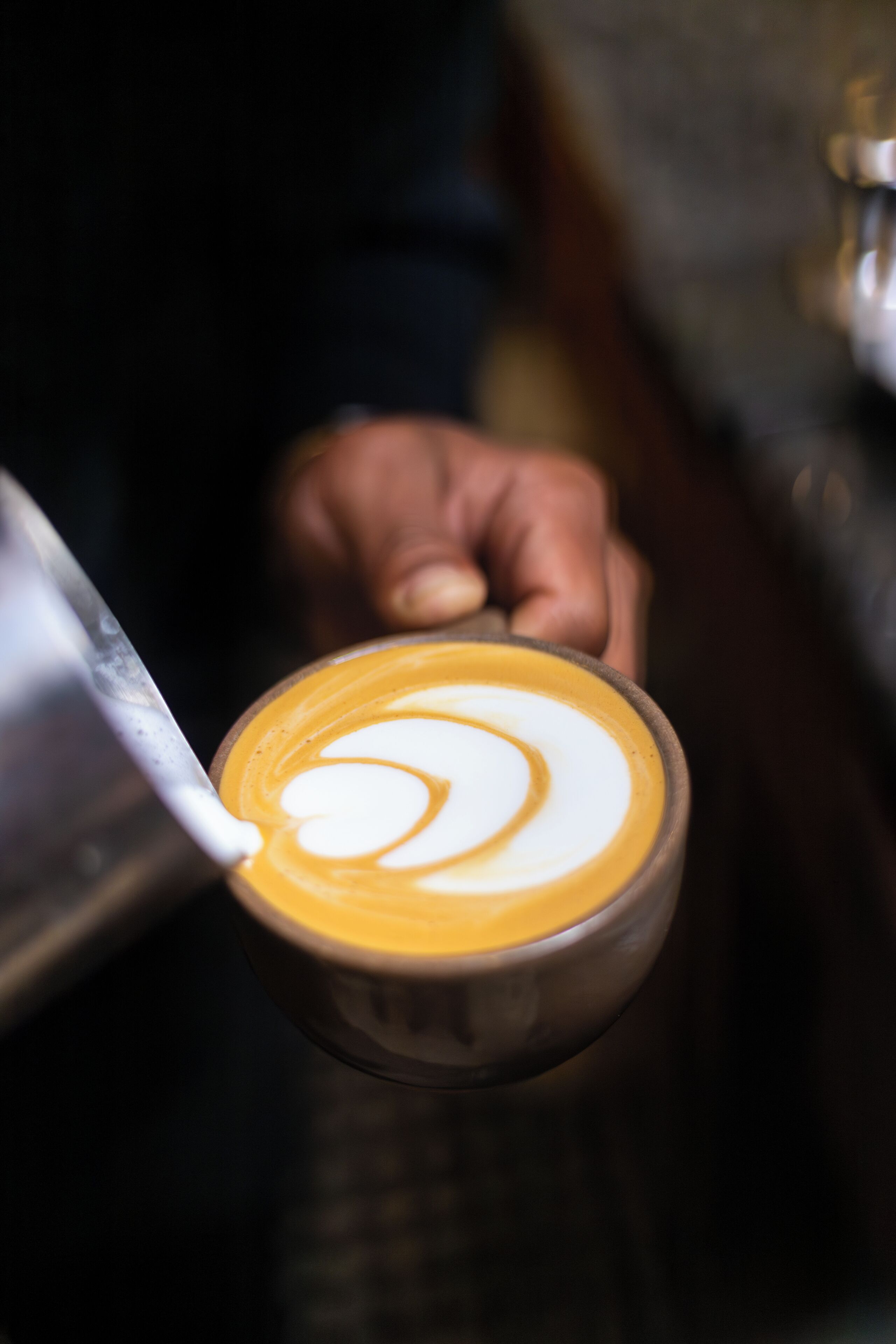 A close-up of a hand pouring milk into a cup of coffee, creating a latte art design.