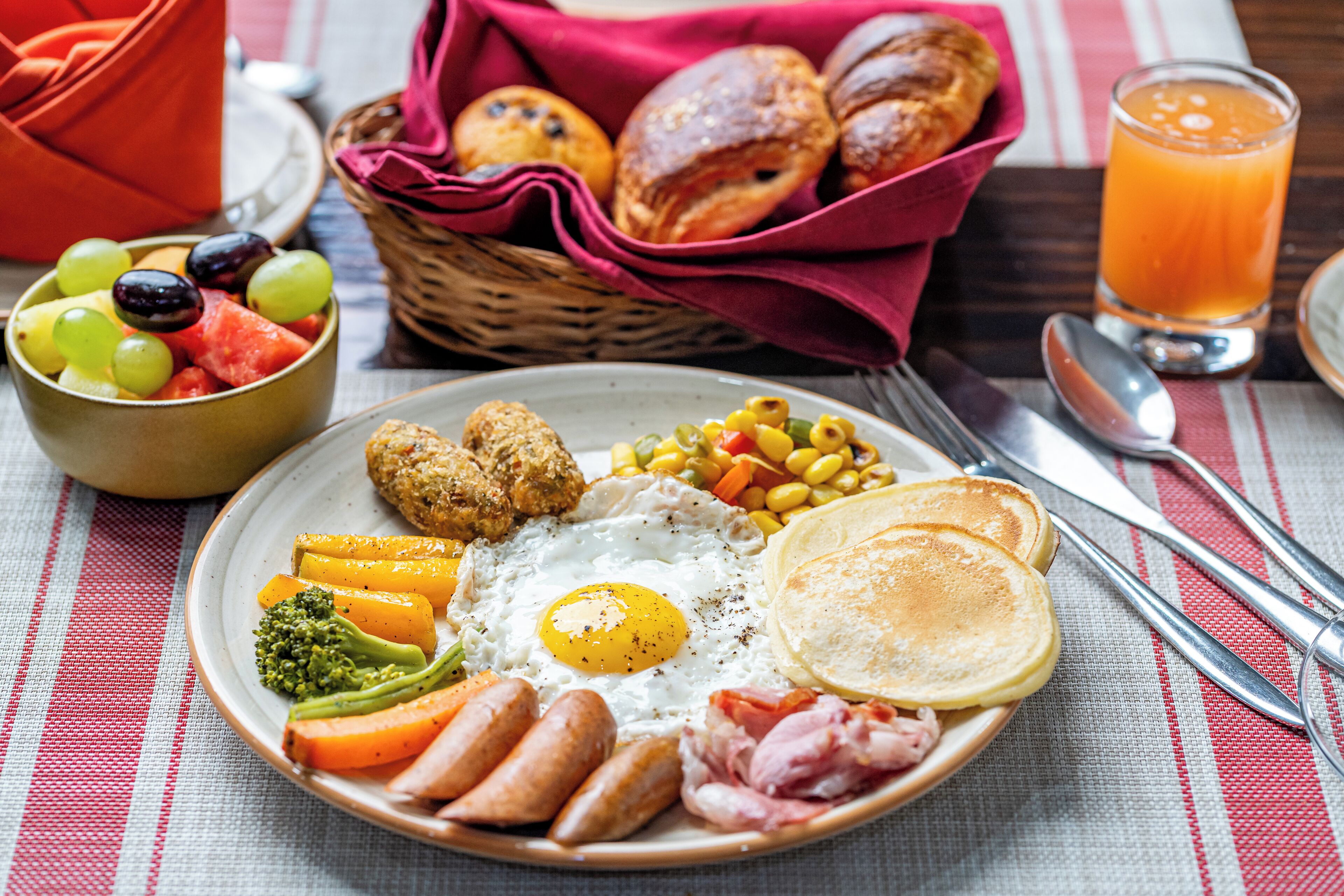 A breakfast plate with eggs, sausages, ham, and vegetables.