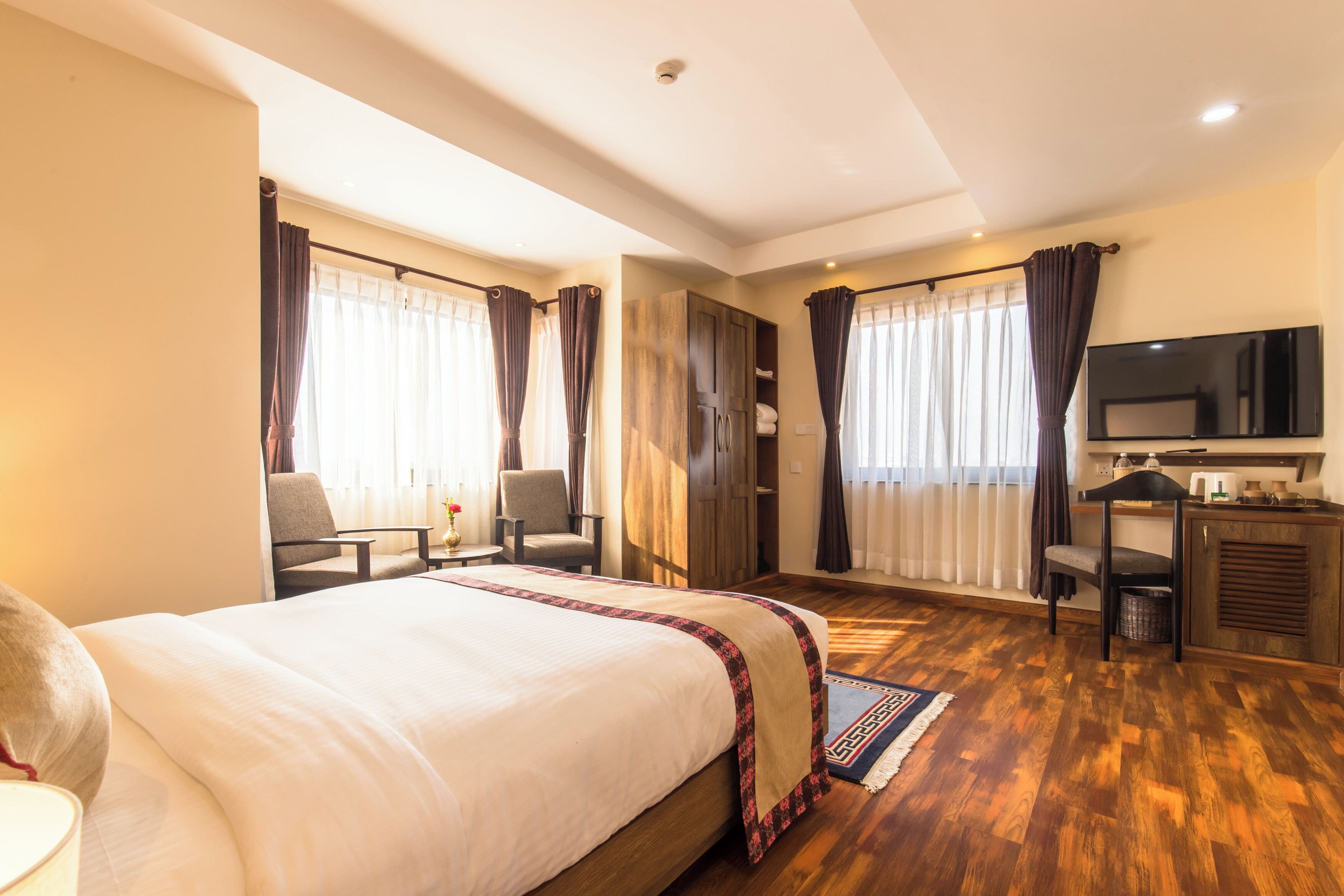 A hotel room with a large bed, two chairs, a desk, a television, and a wardrobe.