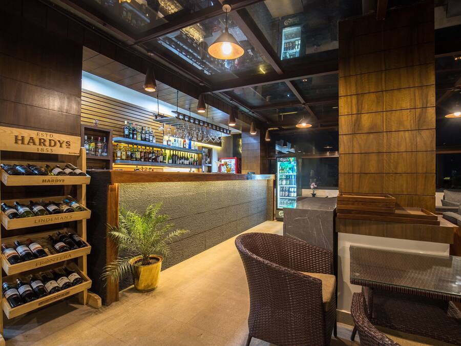 A bar area with wooden shelves displaying various bottles, a seating area with wicker furniture, and a potted plant.