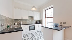 A modern kitchen with white cabinets, a black countertop, and a patterned floor. - The Enya Suite - hiphipstay (Dublin)
