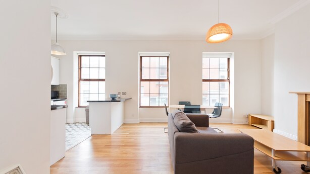 A modern living room with a sofa, a dining table, and a kitchen area in the background. - The Enya Suite - hiphipstay (Dublin)