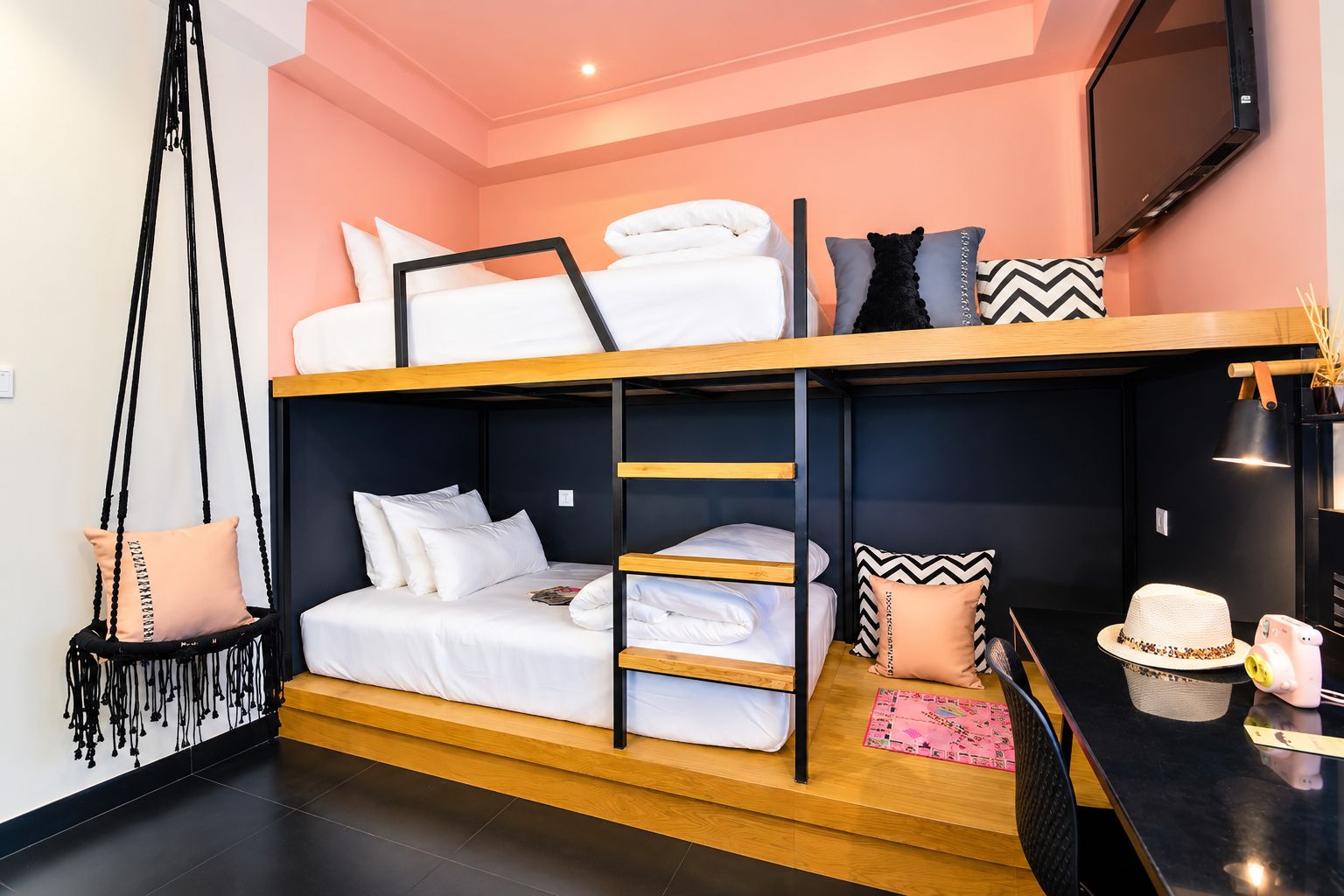 A bunk bed room with a TV, a hanging chair, and a small table with a hat and a piggy bank.
