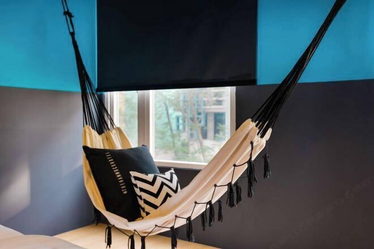A hammock chair with black and white pillows, a window with a view, and a dark blue wall.