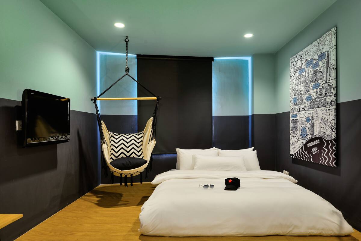 A modern hotel room with a hanging chair, a bed with white linens, and a large wall mural.