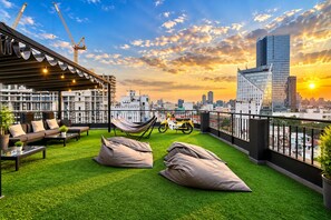 Terraza en la azotea con vistas al horizonte de una ciudad, césped artificial verde, mobiliario exterior y una hamaca.