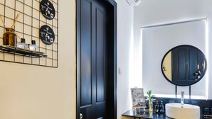 A modern bathroom with a black door, a round mirror, a white sink, and a shelf with toiletries. - The Hammock Hotel Fine Arts Museum (Ho Chi Minh City)