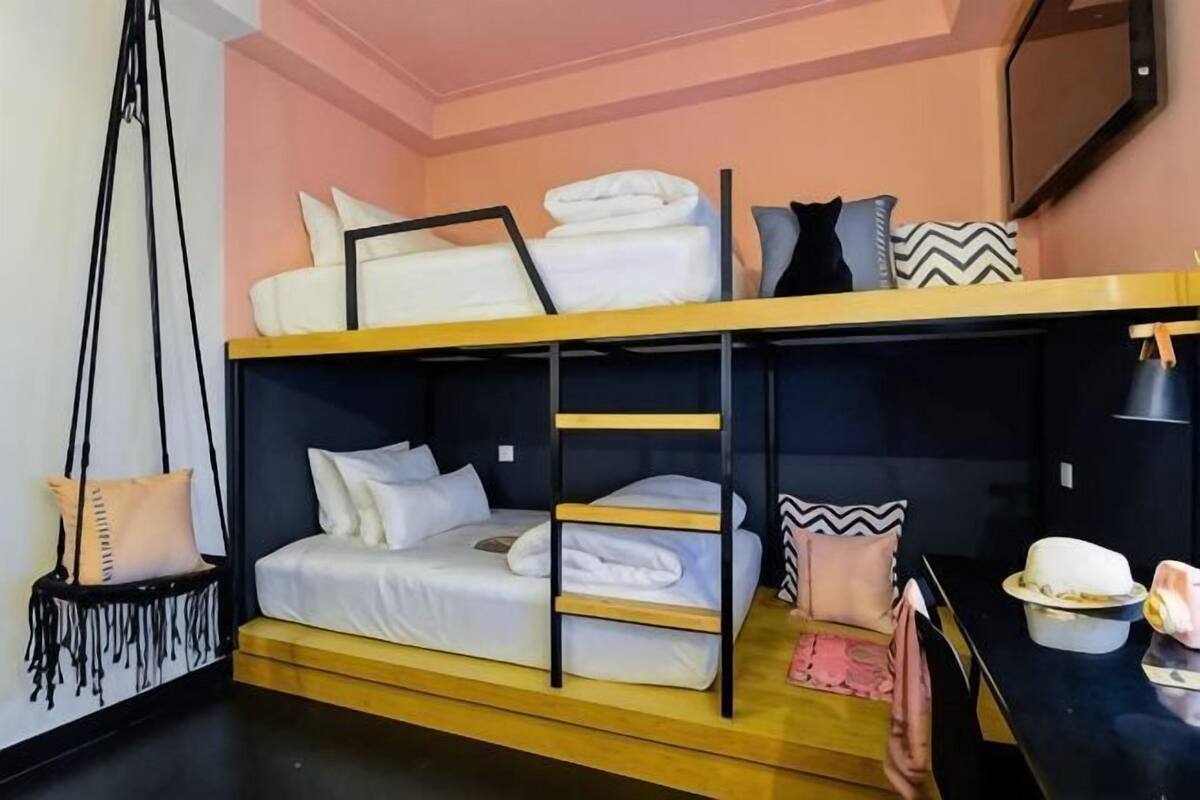 A bunk bed room with a television, a small table with a lamp, and a hanging chair.