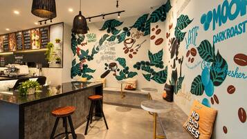 Uma área de bar moderna com balcão, banquetas e um mural na parede com obras de arte sobre café.