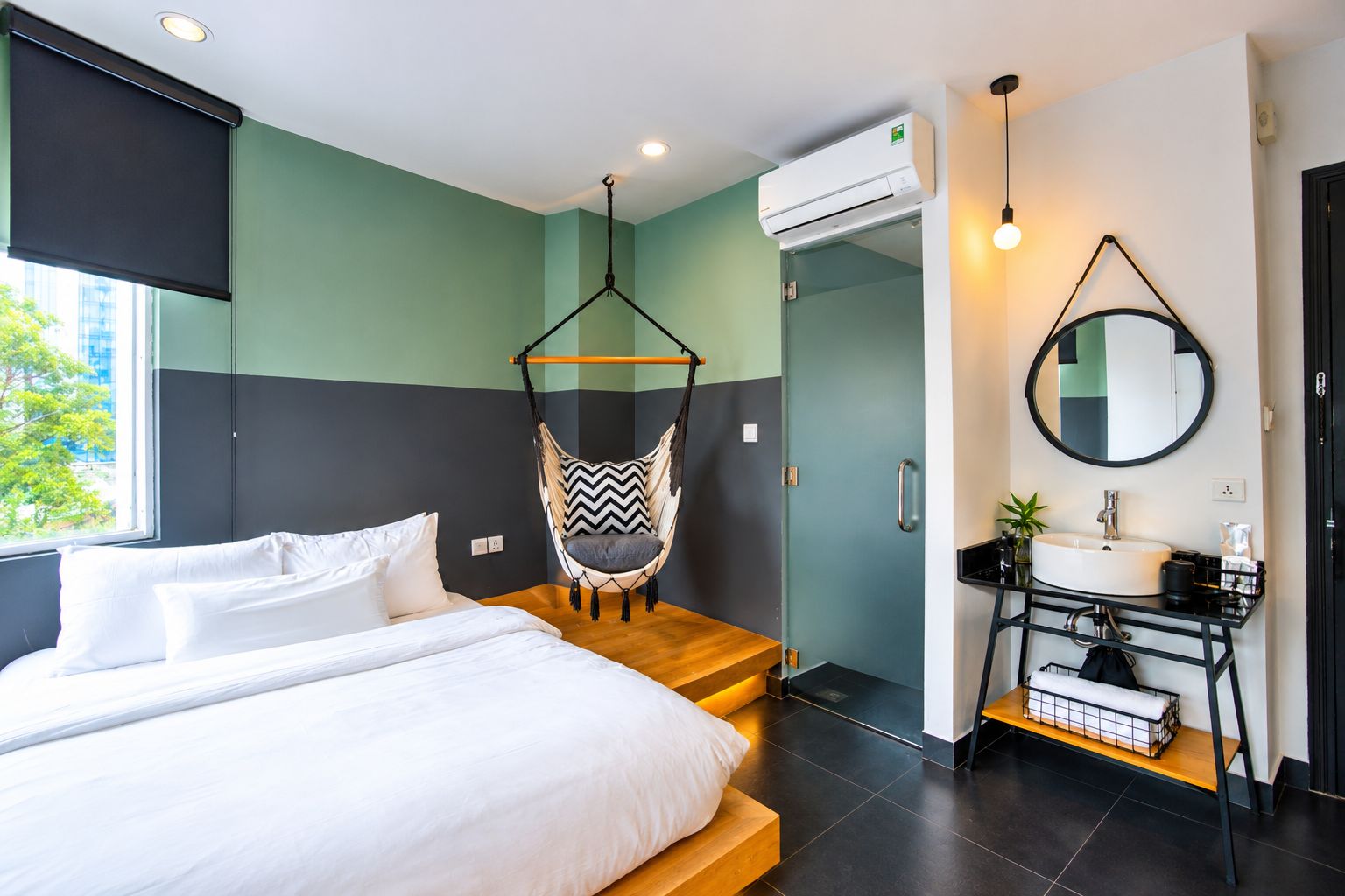 A modern bedroom with a bed, a hanging chair, a bathroom with a sink and mirror, and an air conditioning unit.
