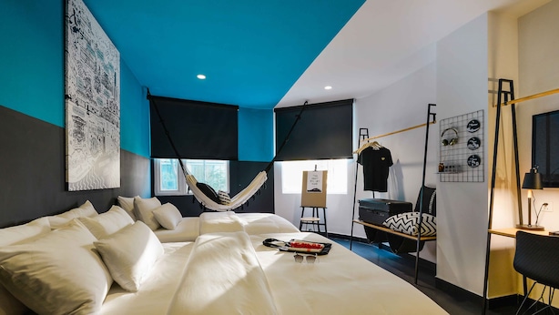A modern bedroom with a large bed, a hammock, a desk, and a chair. - The Hammock Hotel Fine Arts Museum (Ho Chi Minh City)