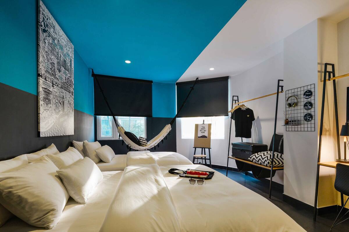 A modern bedroom with a large bed, a hammock, a desk, and a chair.
