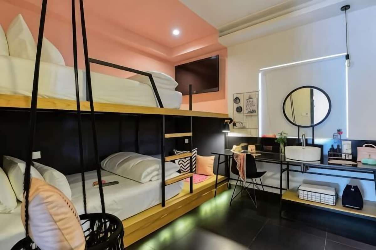 A bunk bed room with a desk, a mirror, and a small table with items.