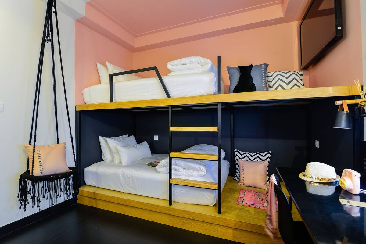 A bunk bed room with a wooden ladder, a hanging chair, and a table with a hat and a camera.