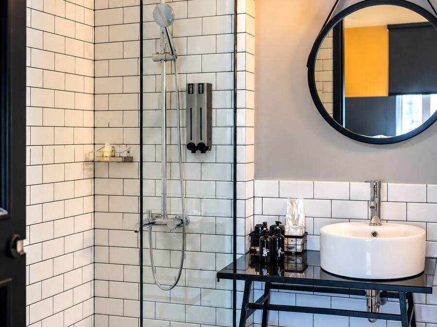 Un baño moderno con ducha envuelta en vidrio, lavamanos blanco sobre encimera negra y un espejo redondo en la pared.