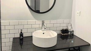 A bathroom with a white sink, black countertop, and a round mirror. - The Hammock Hotel Fine Arts Museum (Ho Chi Minh City)