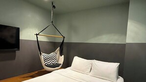 A modern bedroom with a large bed, a hanging chair, and a flat-screen TV mounted on the wall. - The Hammock Hotel Fine Arts Museum (Ho Chi Minh City)