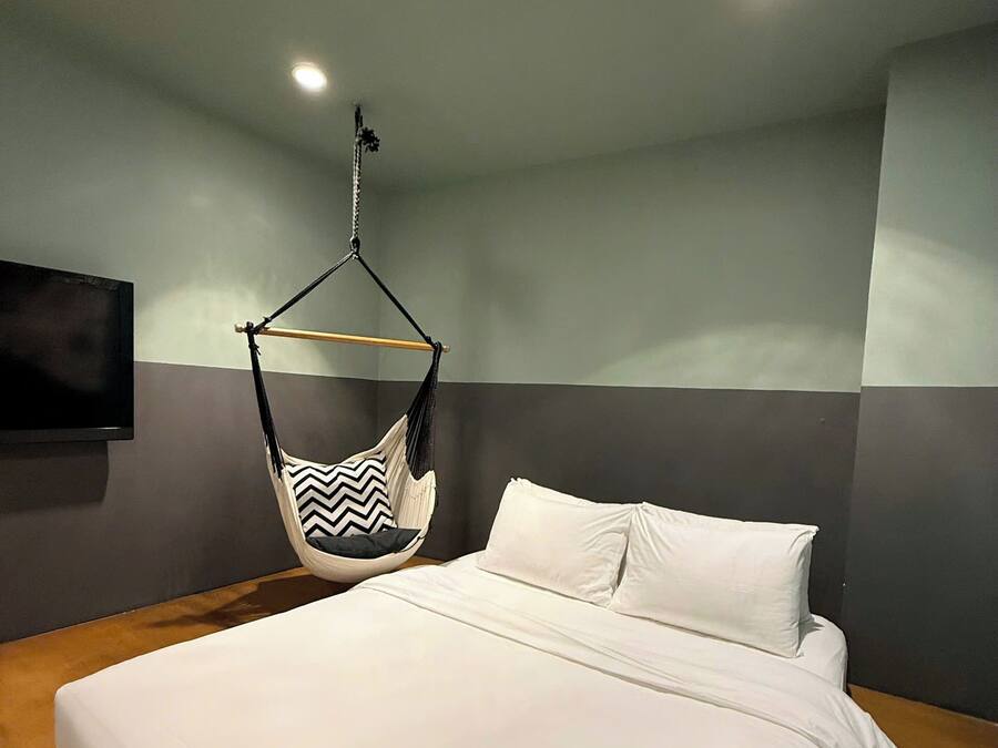 A modern bedroom with a large bed, a hanging chair, and a flat-screen TV mounted on the wall.