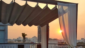A balcony with a sofa and a table, a view of the cityscape, and a sunset. - The Hammock Hotel Fine Arts Museum (Ho Chi Minh City)