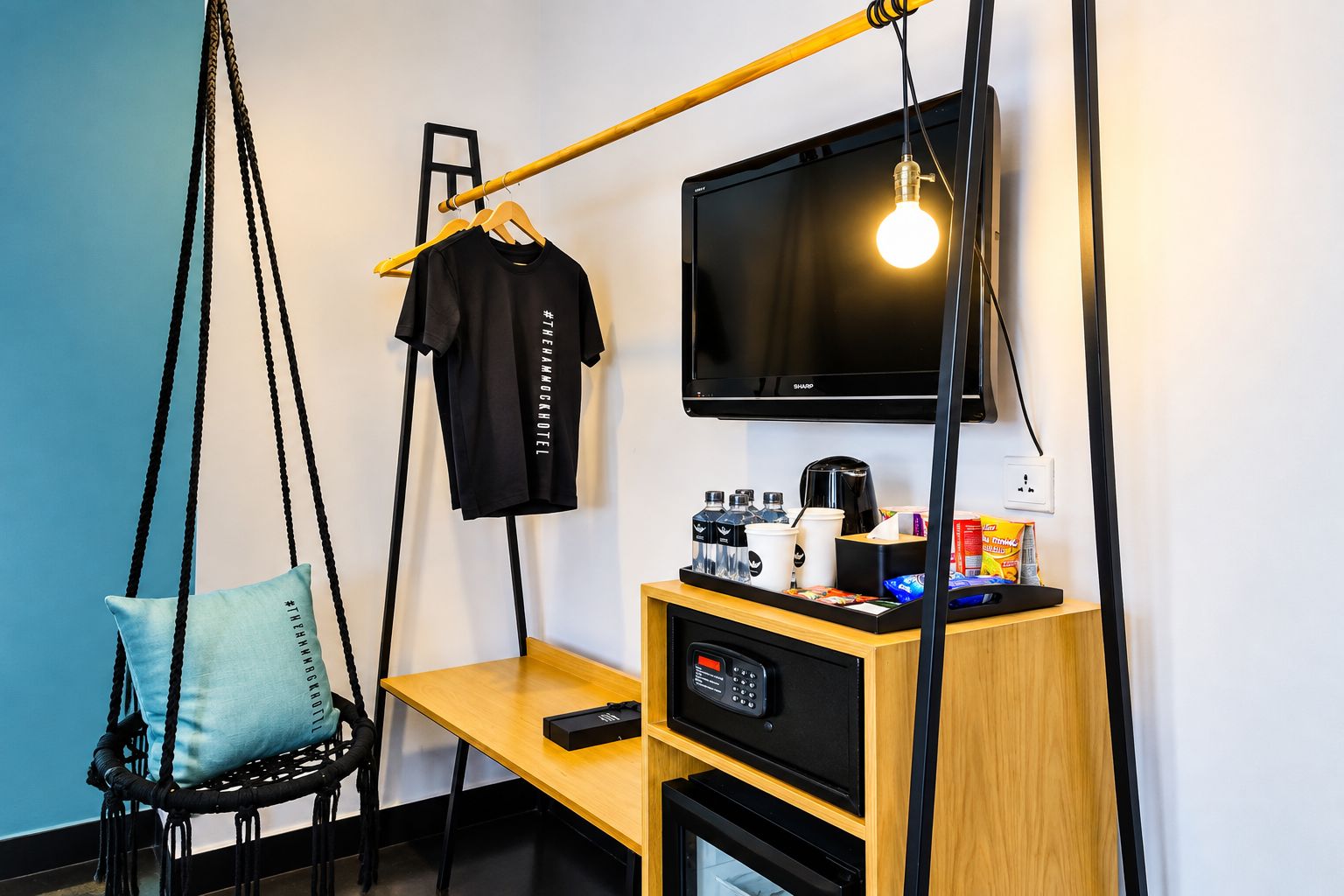 A modern hotel room with a hanging chair, a desk with a coffee machine, a TV, and a remote control.