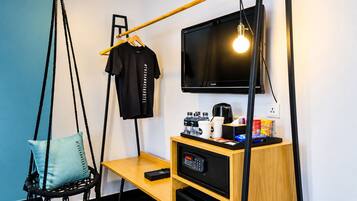 A modern hotel room with a hanging chair, a desk with a coffee machine, a TV, and a remote control.