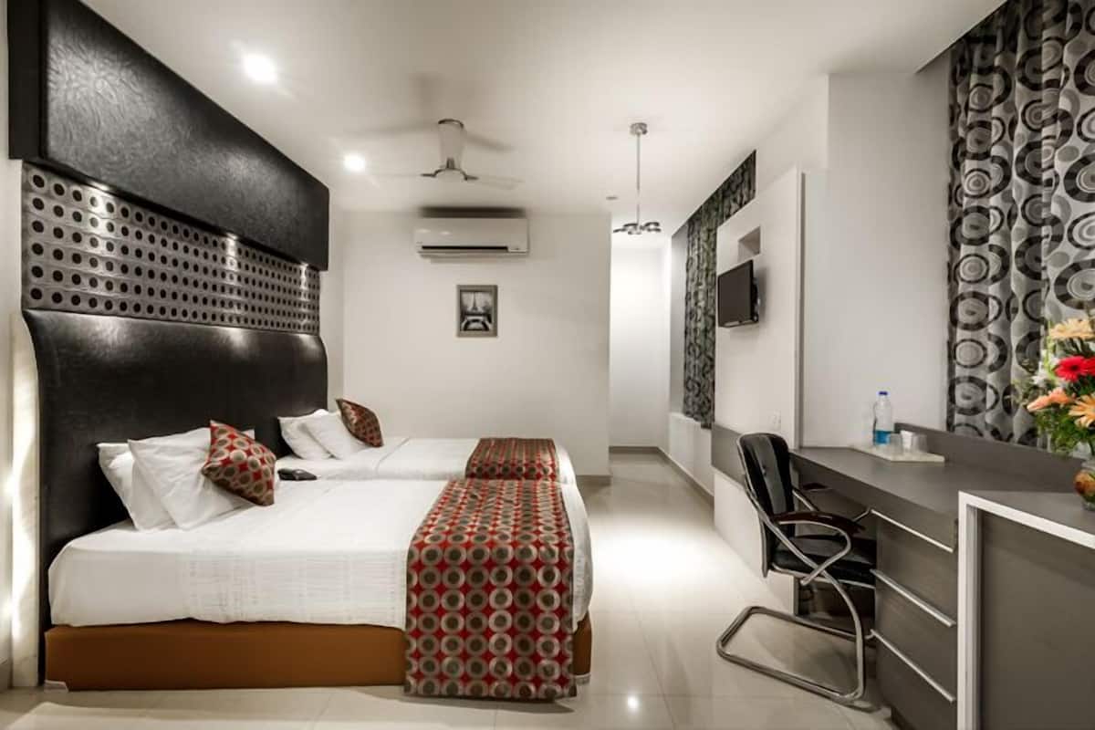 A modern hotel room with two beds, a desk, and a chair.