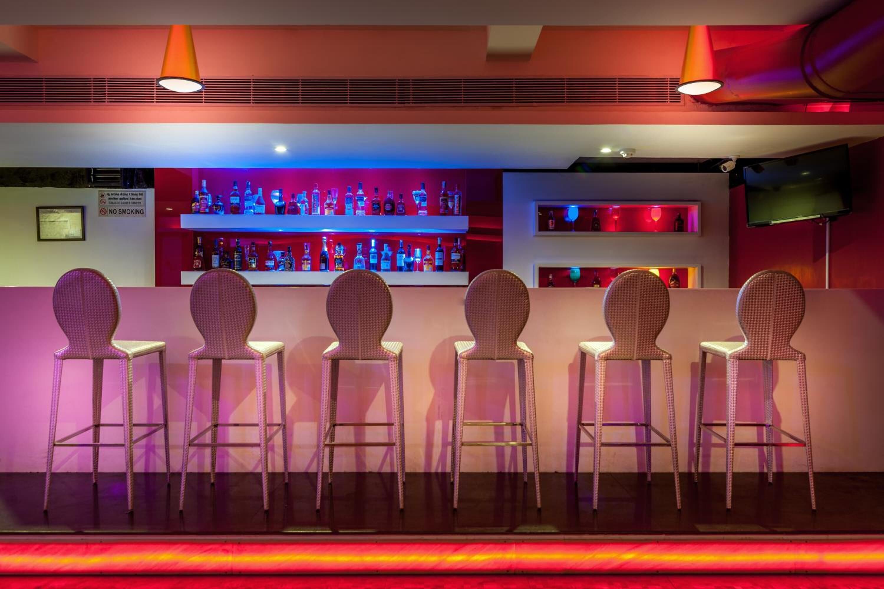 Uma área de bar com uma fileira de cadeiras de vime e uma estante com garrafas de bebidas.