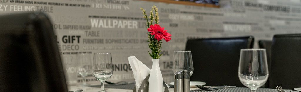 A restaurant table with a vase of flowers, wine glasses, and a menu.