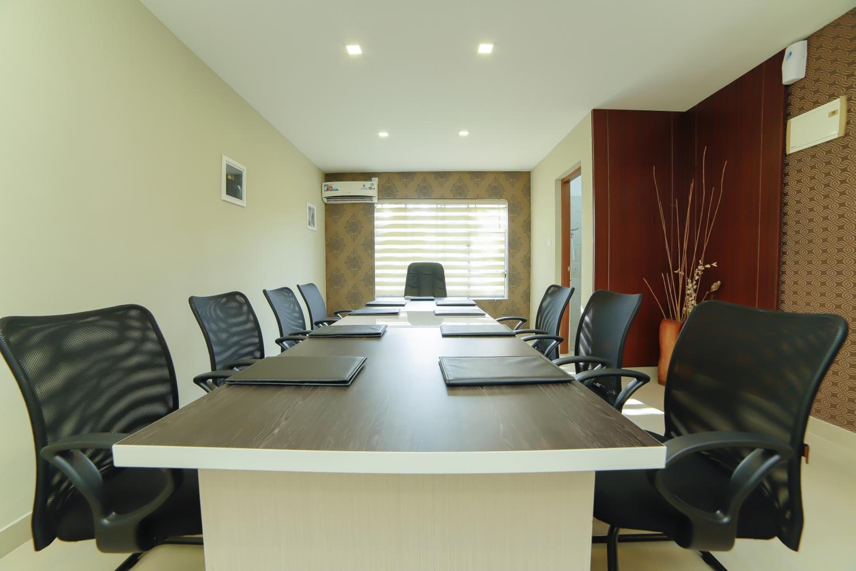 A conference room with a long table, black chairs, and a window with blinds.