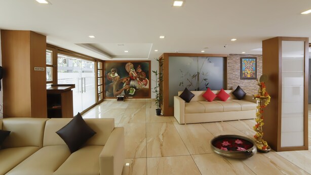 A modern hotel lobby with a beige sofa, a decorative plant, and a wall-mounted phone. - Hotel Sreepathy Indraprastha (Chavakkad)