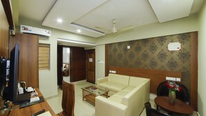 A hotel room with a sofa, a small table, a TV, and a ceiling fan. - Hotel Sreepathy Indraprastha (Chavakkad)