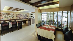 A restaurant with a long dining table, black chairs, and a view through large windows. - Hotel Sreepathy Indraprastha (Chavakkad)