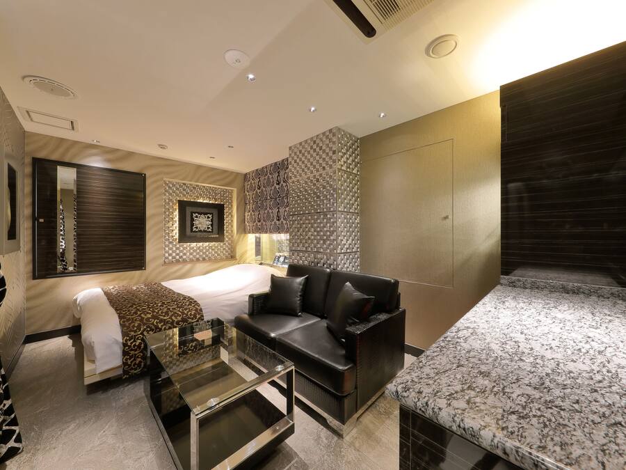 A modern hotel room with a bed, a sofa, a small table, and a marble countertop.