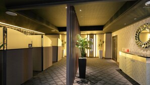 A hotel reception area with a reception desk, a large potted plant, a mirror on the wall, and a patterned carpet. - Hotel Cherena - Adult Only (Kunitachi)