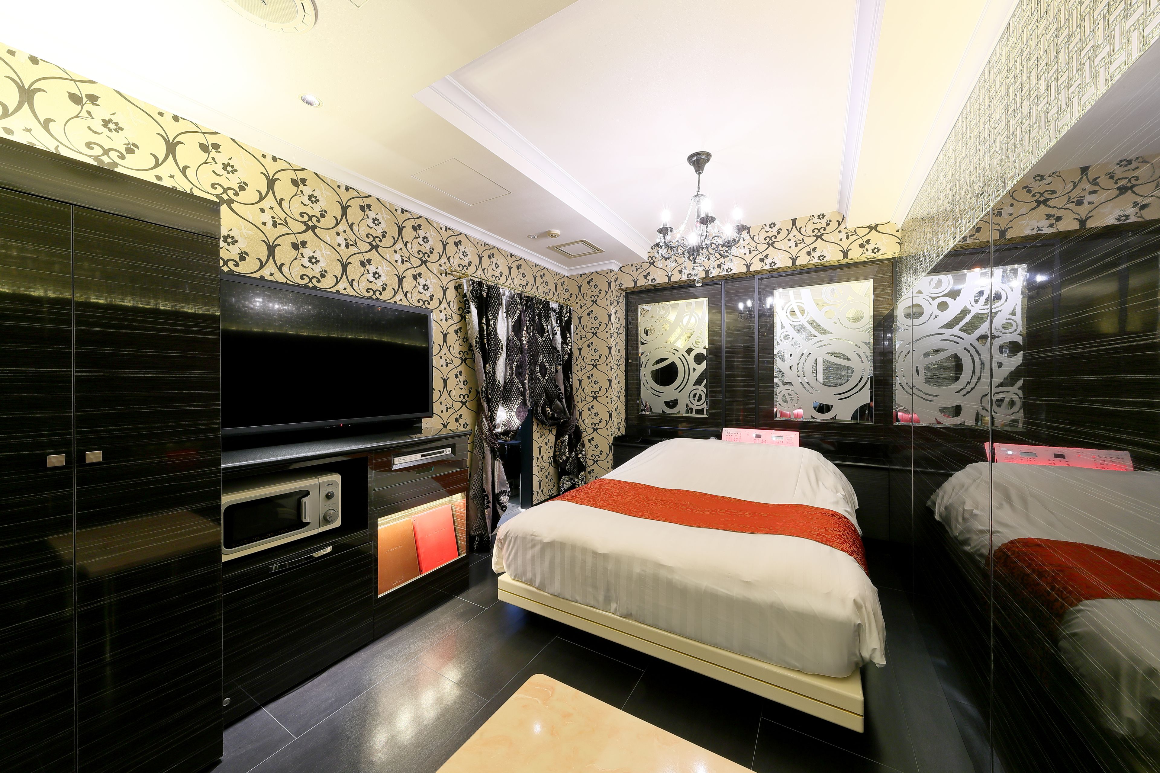 A modern hotel room with a large bed, a flat-screen TV, a vanity with a mirror, and a built-in oven.