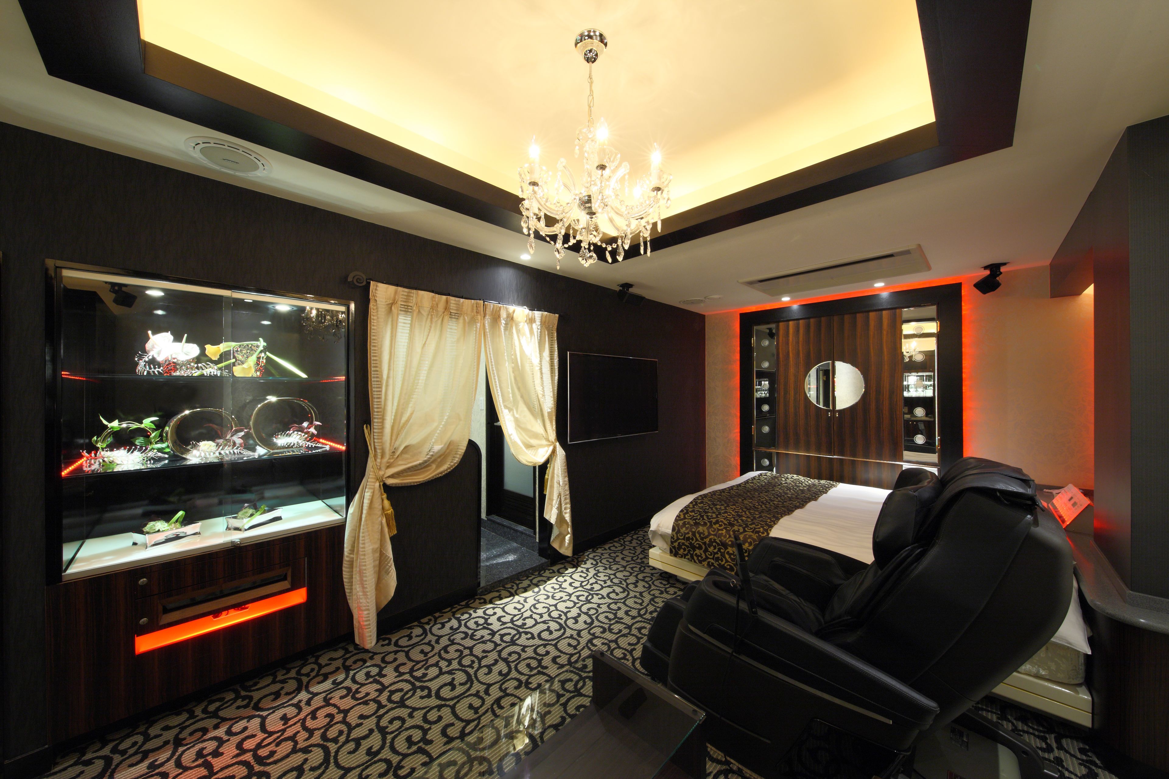 A modern hotel room with a large aquarium, a massage chair, and a bed with a patterned headboard.