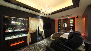 A modern hotel room with a large aquarium, a massage chair, and a bed with a patterned headboard.