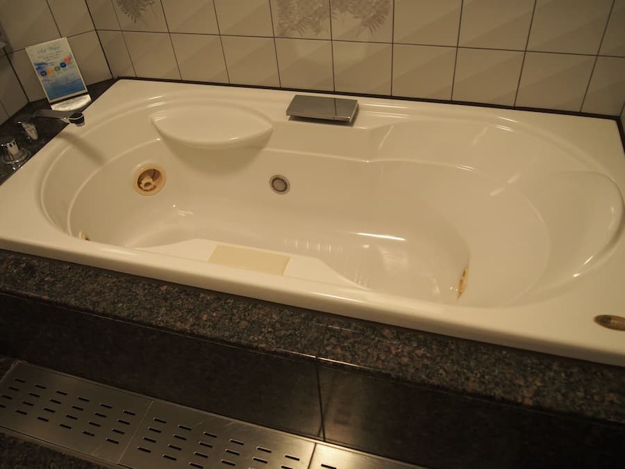 A large, rectangular bathtub with a built-in seat, a small shelf, and a drain.