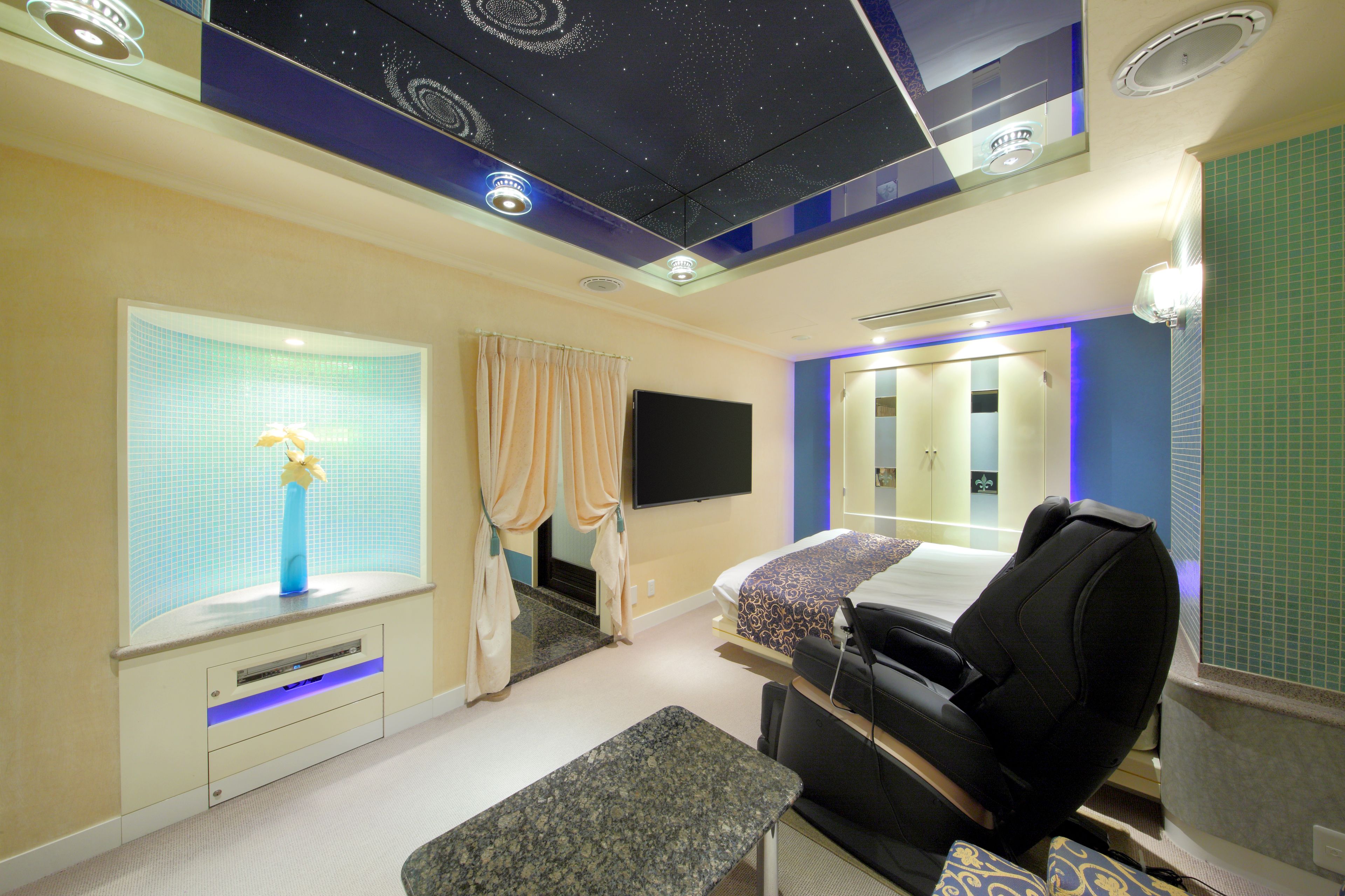 Una habitación de hotel con cama, sillón de masajes, televisor y ventana con cortinas.